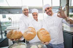 Team of bakers smiling at camera holding bread