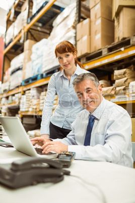 Warehouse management talking and looking at laptop