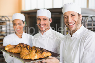 Team of bakers smiling at camera with trays of croissants