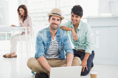 Smiling colleagues sitting on the floor using laptop