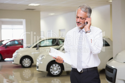 Smiling businessman on the phone holding clipboard