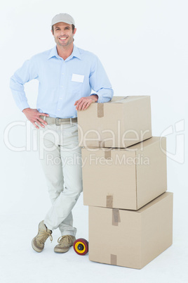 Confident delivery man leaning on stacked cardboard boxes