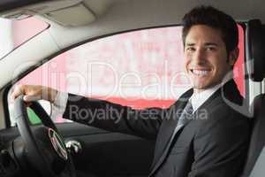 Smiling businessman at the wheel sitting in a car for sale