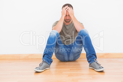 Casual man sitting on floor covering his face at home