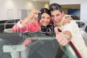 Smiling couple giving thumbs up and holding car key