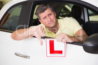 Man gesturing thumbs down holding a learner driver sign