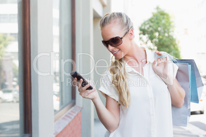 Pretty blonde texting and holding shopping bags