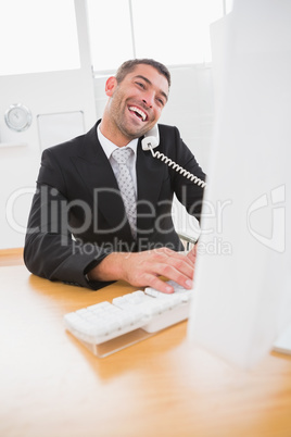 Smiling businessman working and phoning at his desk