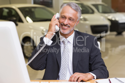 Smiling businessman using phone in front of computer