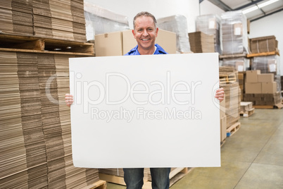 Smiling warehouse worker holding large white poster