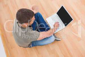 Casual man sitting on floor using laptop at home