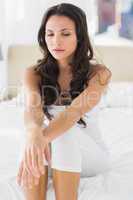 Worried brunette sitting on bed