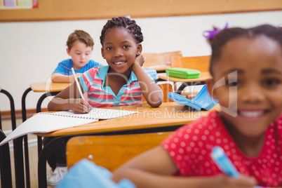 Cute pupils writing at desk in classroom