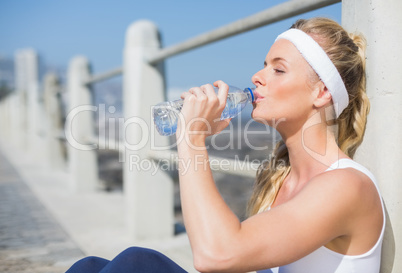 Fit blonde sitting on the pier drinking water