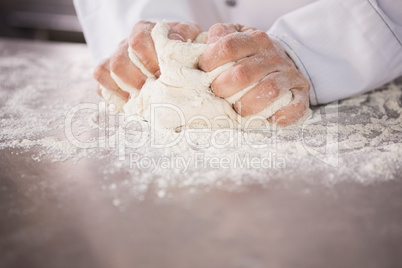 Close up of baker kneading dough on counter