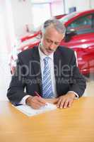 Focused salesman writing on clipboard at his desk