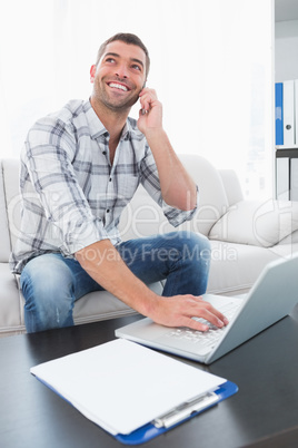 Smiling man on a phone with a laptop at home