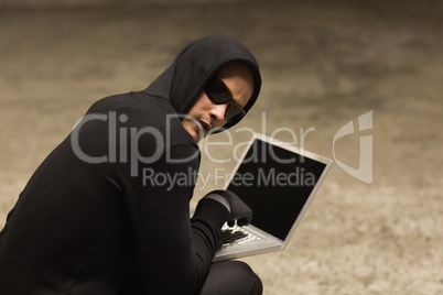 Hacker in hooded jumper using laptop