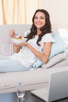 Pretty brunette eating salad on couch