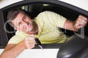 Smiling man holding a car key sitting in his car