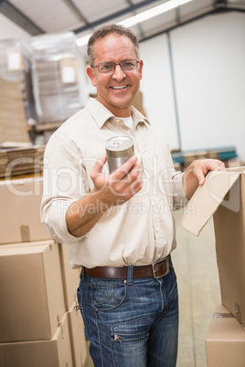 Smiling warehouse worker holding metal tin can