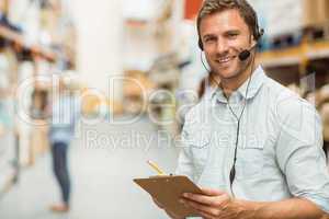 Warehouse manager wearing headset writing on clipboard