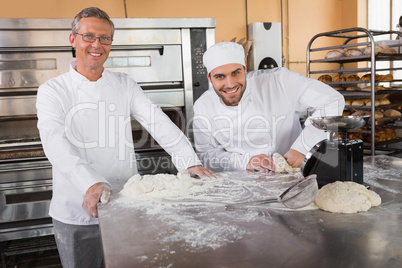 Smiling baker kneading dough next to his colleague