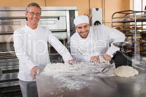 Smiling baker kneading dough next to his colleague