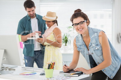 Smiling woman taking note in front of her colleagues