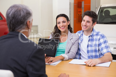 Smiling couple talking with a car dealer