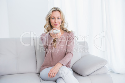 Smiling blonde on couch changing tv channel