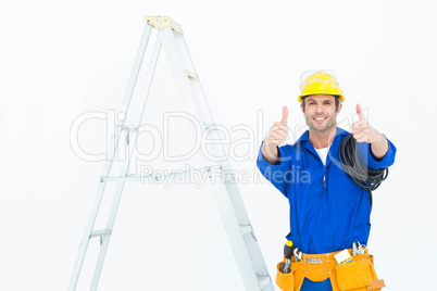 Happy electrician gesturing thumbs up by ladder