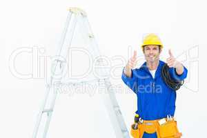 Happy electrician gesturing thumbs up by ladder