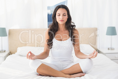 Calm brunette doing yoga on bed