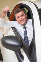 Smiling man holding a car key sitting in his car