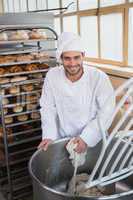 Smiling baker preparing dough in industrial mixer