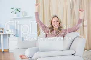 Smiling blonde cheering and using laptop