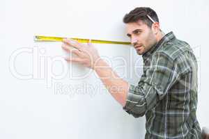 Carpenter measuging white wall with measure tape