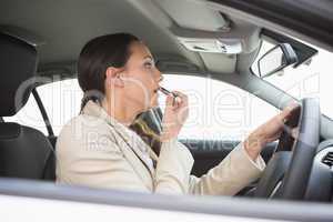 Businesswoman using mirror to put on lipstick while driving
