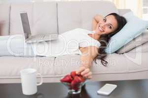 Pretty brunette lying on couch using laptop