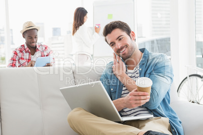 Businessman phoning and holding laptop on sofa