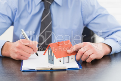 Businessman taking notes and holding miniature house