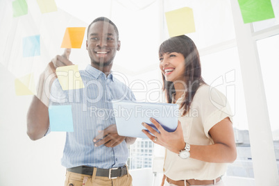 Smiling teamwork reading sticky notes and using tablet