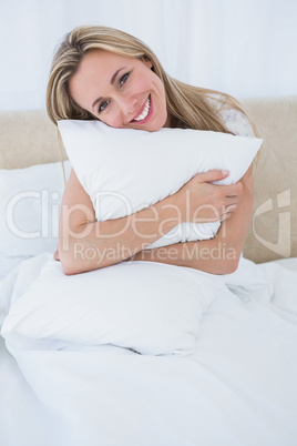 Smiling blonde holding cushion in bed