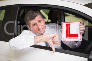 Man gesturing thumbs down holding a learner driver sign