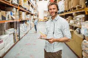 Warehouse manager wearing headset writing on clipboard