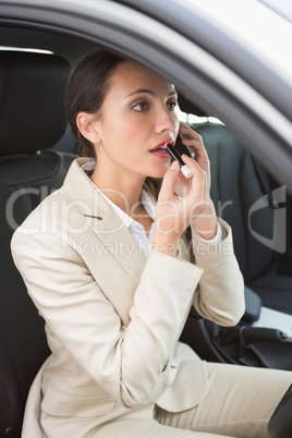 Businesswoman having a phone call while putting on lipstick