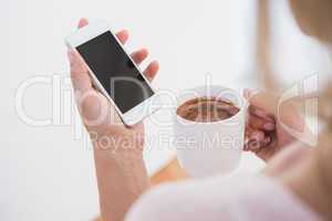 Blonde holding smartphone and mug of hot chocolate