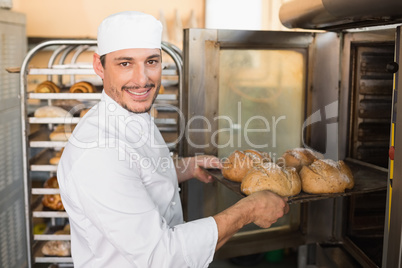 Happy baker taking out fresh loaves