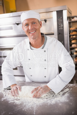 Smiling baker kneading dough on counter